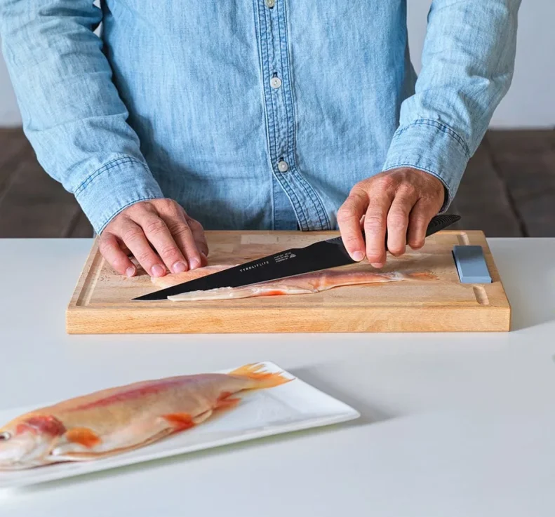 Mann im blauen Hemd filetiert einen Fisch mit einem schwarzen Filetiermesser von Tyrolit Life Darkline Messerserie