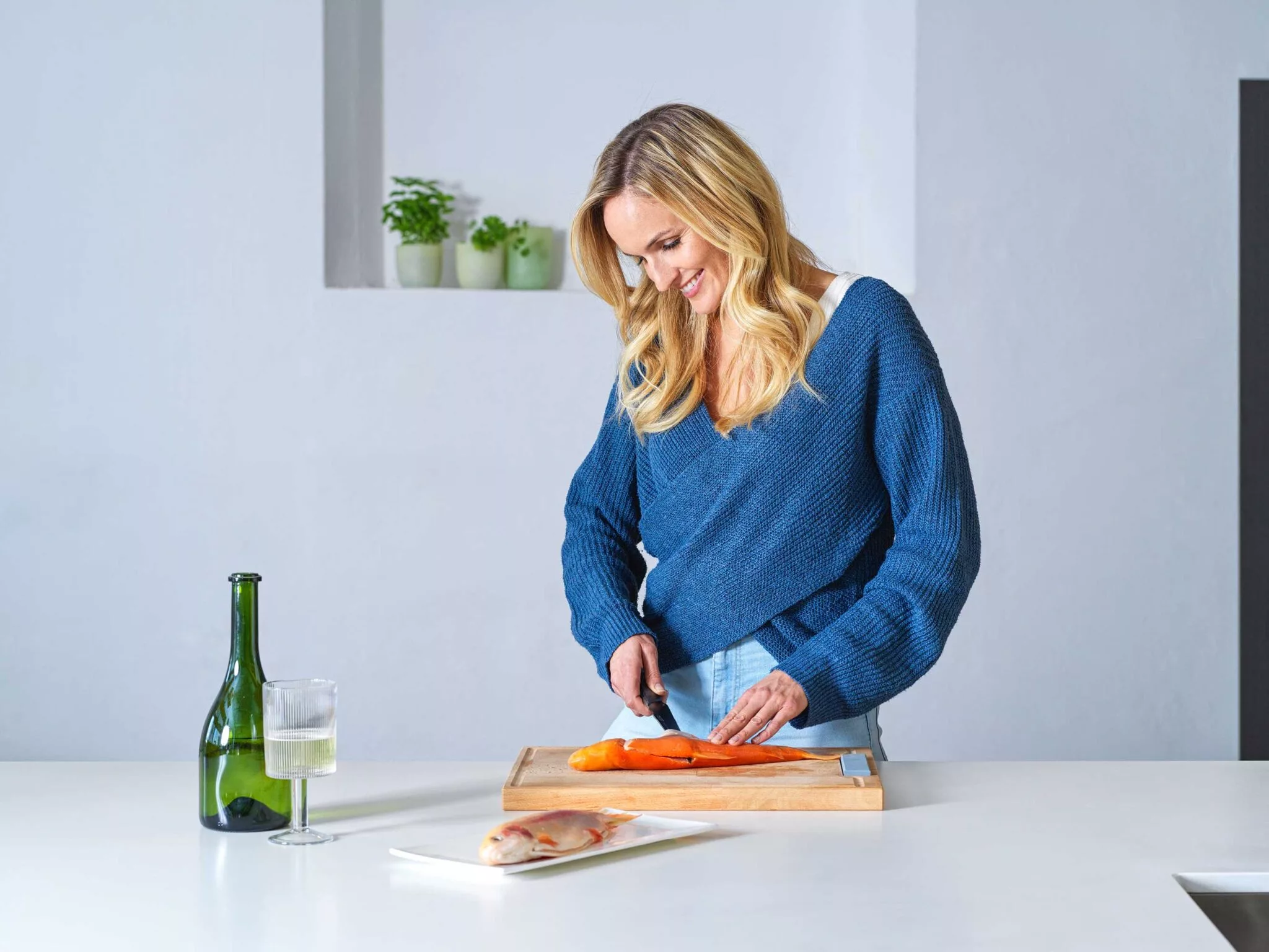 Blonde Frau mit blauem Pollover filetiert einen Lachs in der Küche mit Küchenmesser von Tyrolit Life